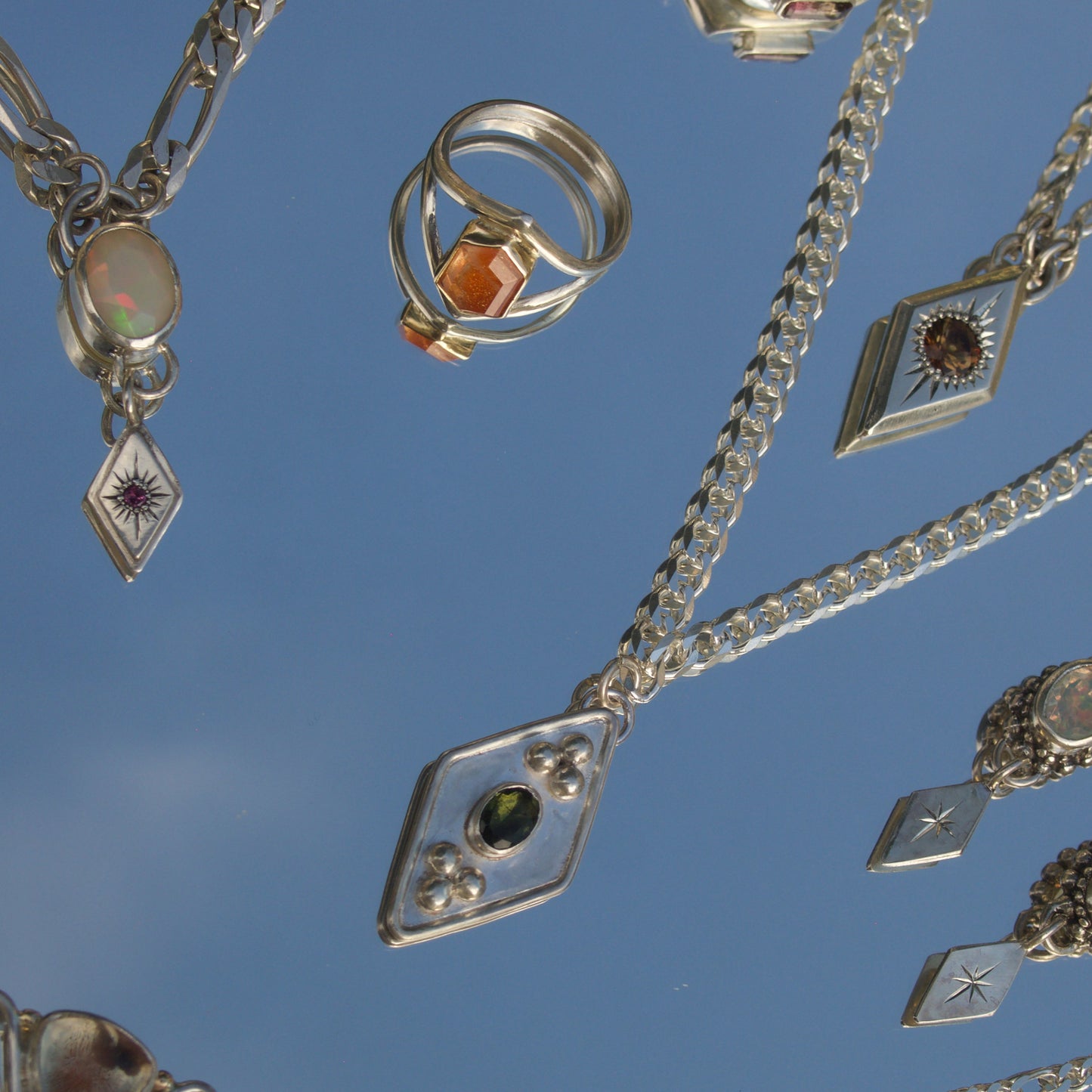 Collection of silver jewelry with gemstones against a blue sky background orange sunstone