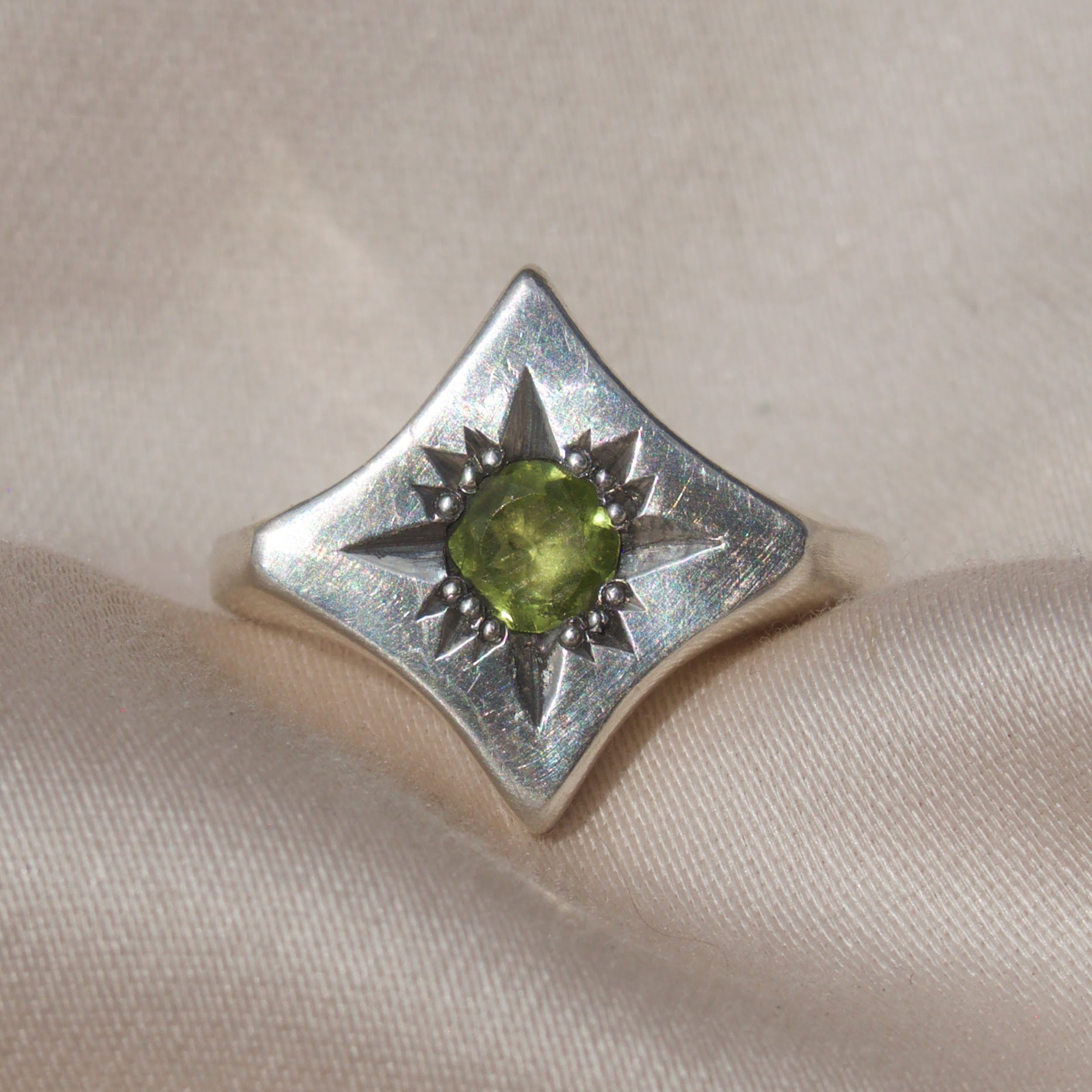 Silver ring with a green peridot gemstone on a sleek cream colored backround