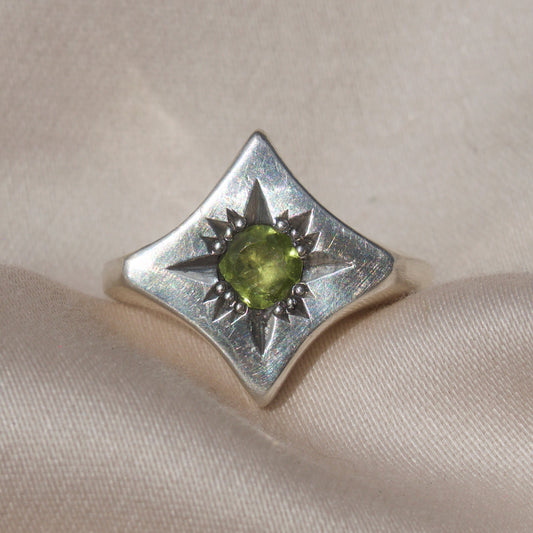 Silver ring with a green peridot gemstone on a sleek cream colored backround