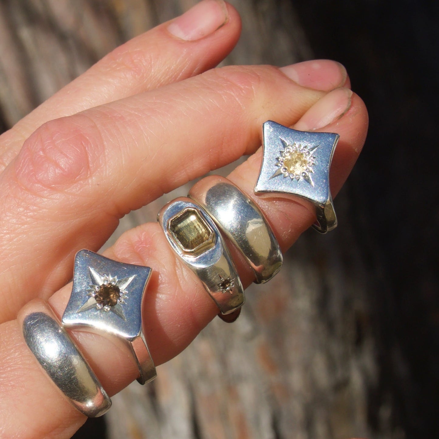 Hand wearing three silver rings with star-shaped designs on a blurred natural background