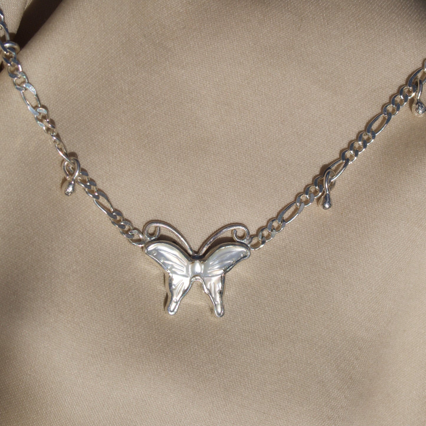 Silver butterfly necklace on a beige fabric background