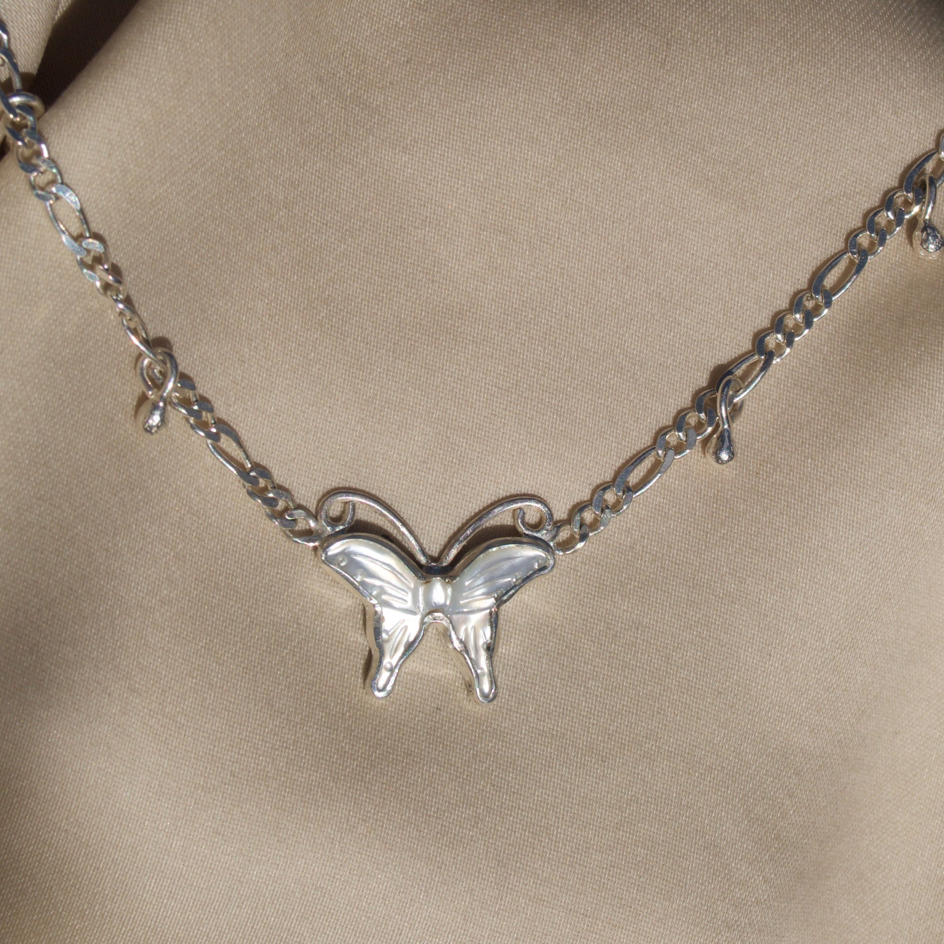 Silver butterfly necklace on a beige fabric background