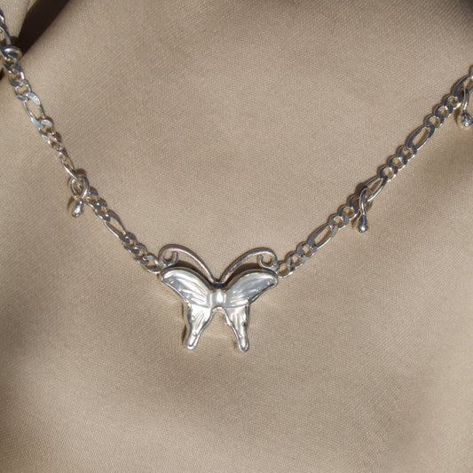 Silver butterfly necklace on a beige fabric background