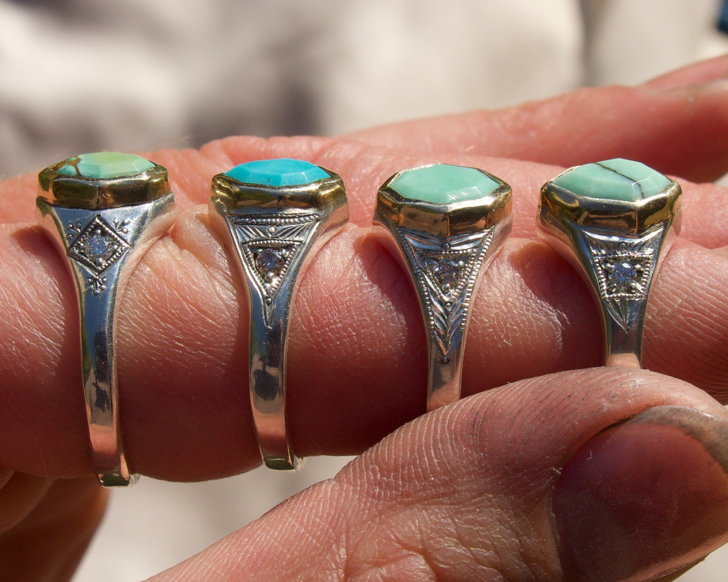 Four rings with turquoise stones and gold accents on a hand.